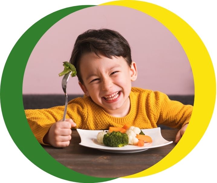 Child sat at table eating a plate of vegetables and smiling
