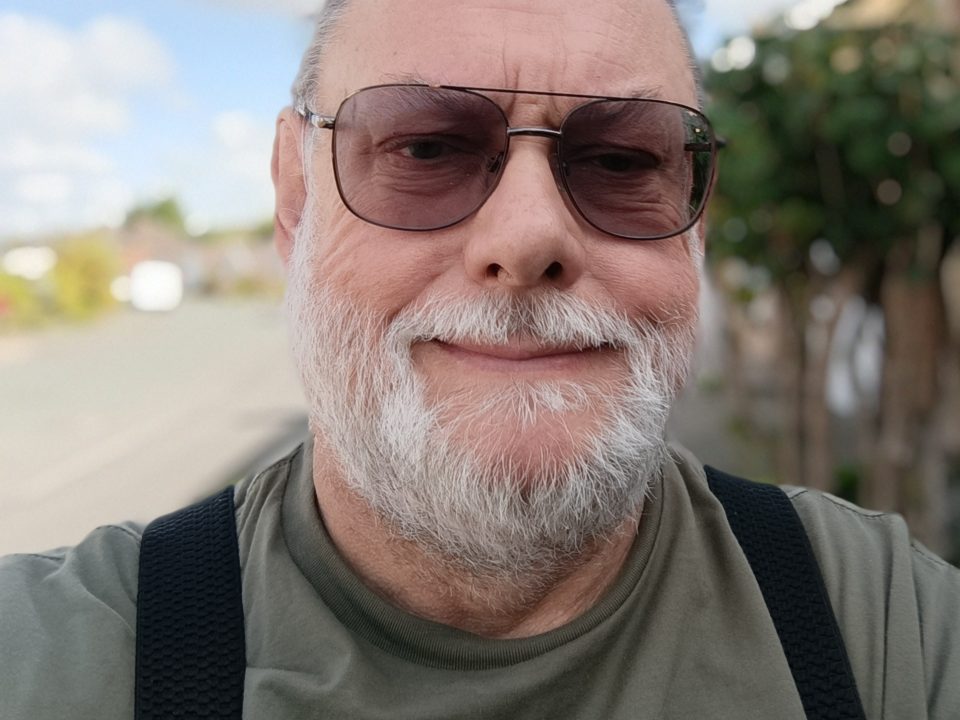 Photo of John Crouchley walking along the street and smiling at the camera.