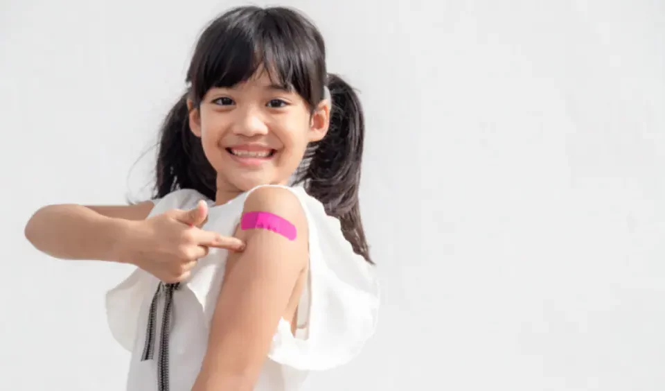 A girl with a pink plaster on her arm after had a jab.