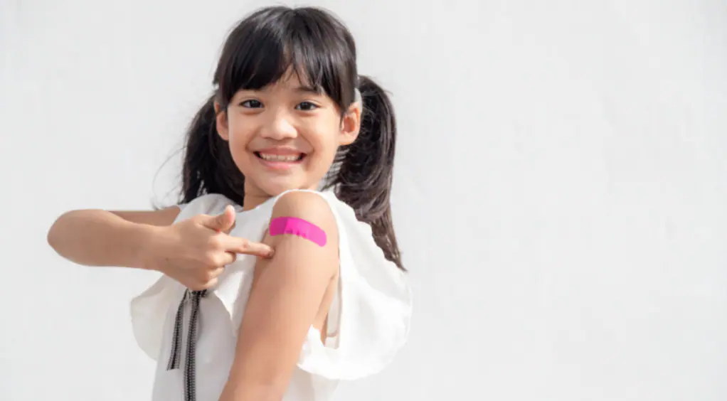 A girl with a pink plaster on her arm after had a jab.